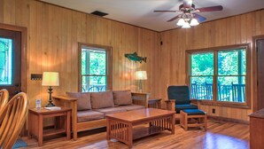 A wooden-paneled room with a sofa, two chairs, a coffee table, and a ceiling fan.