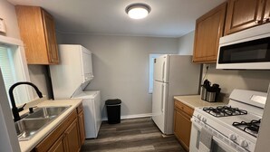 A compact kitchen with wooden cabinets, a stainless steel sink, a white refrigerator, a stove, and a microwave. - COZY COTTAGE NEAR CEDAR POINT/ KALAHARI /SUMMIT RACEWAY (Norwalk)
