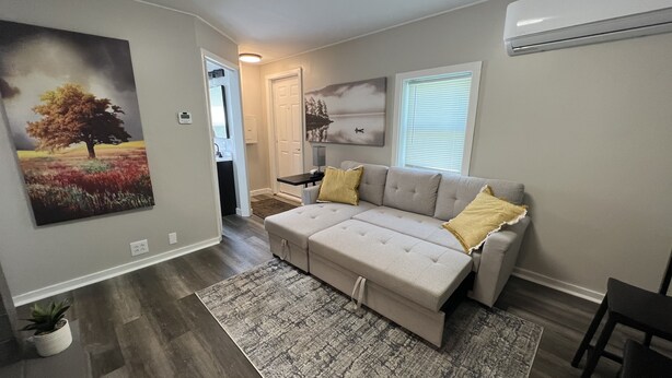 A living room with a beige sectional sofa, a patterned rug, and a painting of a tree. - COZY COTTAGE NEAR CEDAR POINT/ KALAHARI /SUMMIT RACEWAY (Norwalk)