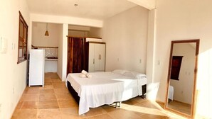 Un dormitorio con una cama, un espejo y una kitchenette al fondo.