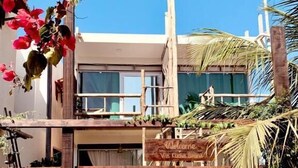 Una puerta de madera con un letrero que dice 'Welcome', un edificio moderno con ventanales grandes y plantas tropicales.
