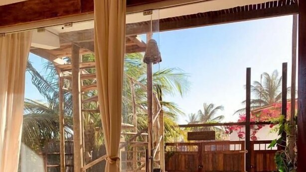 Una habitación con puerta de vidrio corredera que da a un espacio exterior con mesa y sillas de madera, una pérgola y una valla de madera.