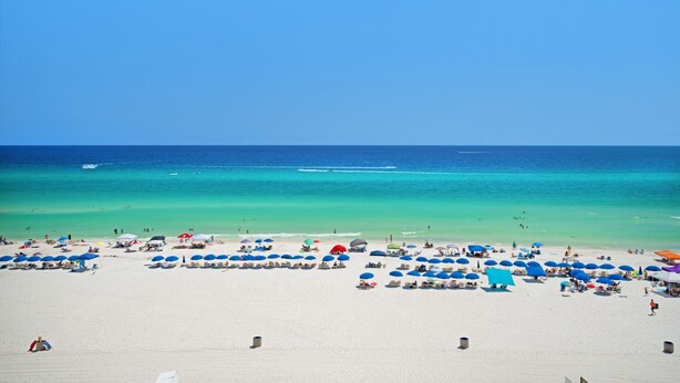 A beach with numerous umbrellas and sun loungers, a clear blue sky, and a calm sea.