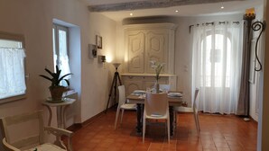 A dining area with a table set for two, chairs, a potted plant, and a cabinet with decorative doors.