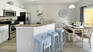 A modern kitchen with white cabinets, a granite countertop, a stainless steel refrigerator, and a central island with bar stools. - Bright contemporary end resort home with private pool - Terra Verde Resort! (Kissimmee)