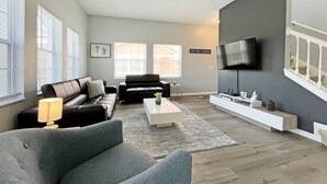 A modern living room with a sofa, coffee table, and a flat-screen TV mounted on the wall. - Bright contemporary end resort home with private pool - Terra Verde Resort! (Kissimmee)
