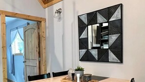 Un espace repas comprenant une table en bois, des chaises noires et une œuvre d’art murale aux motifs géométriques.