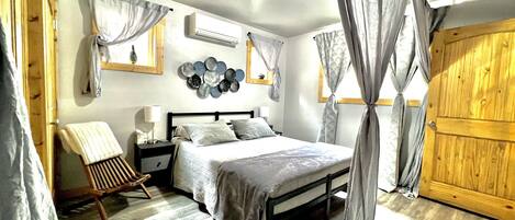 A bedroom with a bed, nightstand, chair, and curtains.