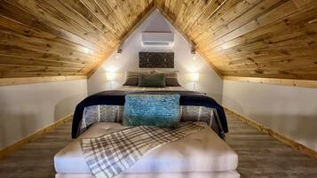 Un dormitorio ático acogedor con techo inclinado, una cama con ropa de cama estampada, un banco y dos lámparas de noche.