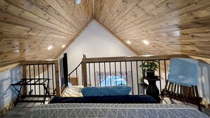 Une chambre avec un plafond en pente, un lit recouvert d’une couvre-lit à motifs, une plante en pot et une vue sur l’extérieur.