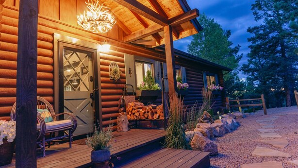 Une cabane en rondins avec une terrasse en bois, un banc et un foyer.