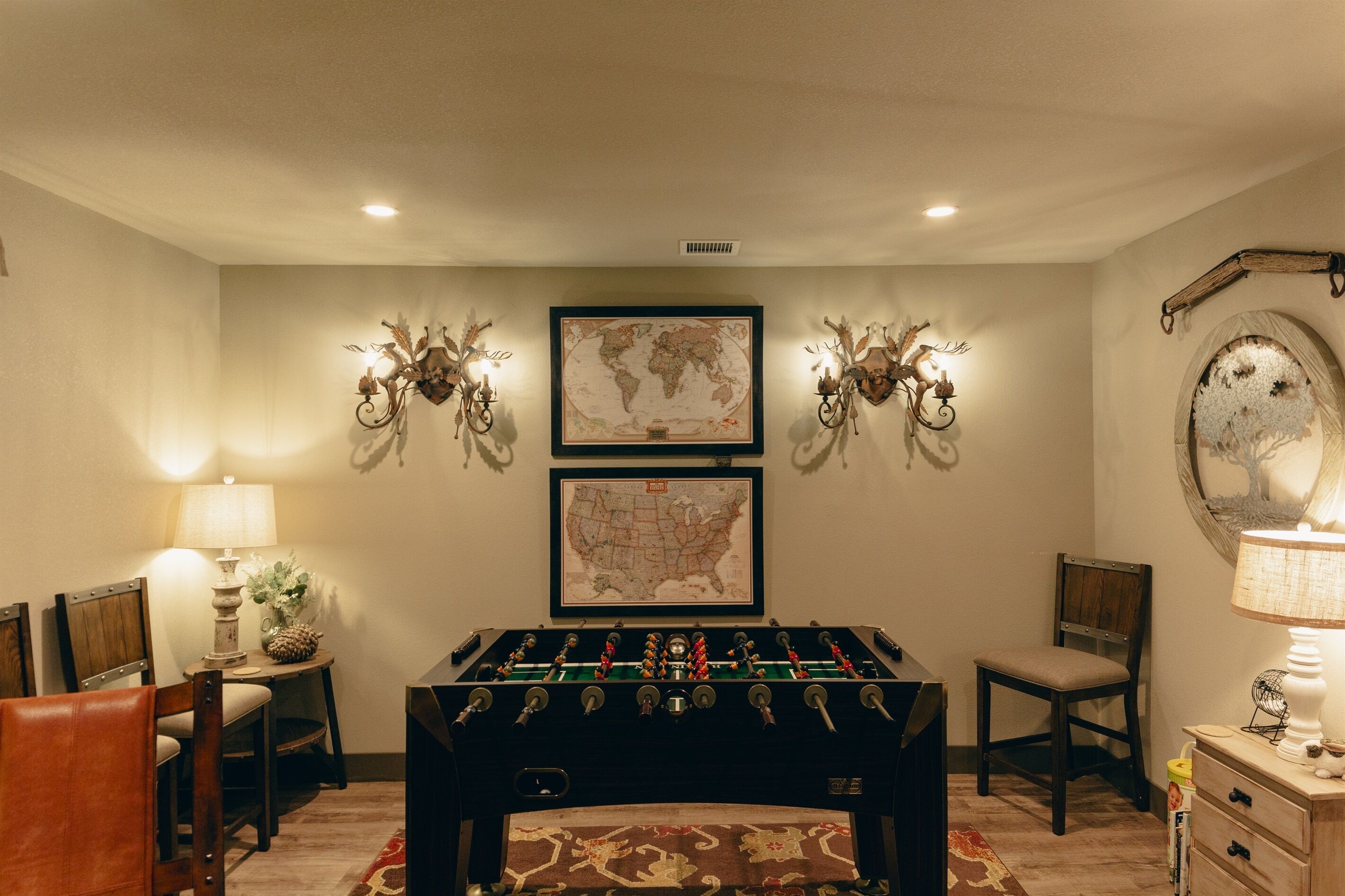 A room with a foosball table, two wall-mounted decorative lights, a world map, and a rustic mirror.