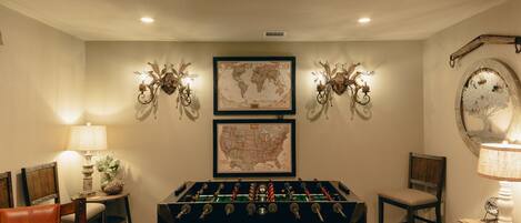 A room with a foosball table, two wall-mounted decorative lights, a world map, and a rustic mirror.
