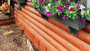 Une cabane en rondins dotée d’une véranda, de balustrades en bois et de jardinières ornées de fleurs violettes et blanches.