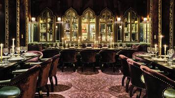 A formal dining room with velvet chairs, a long table, and a mirrored wall with shelves.