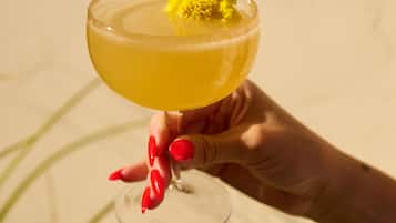 A hand holding a cocktail glass with a yellow drink and a garnish.