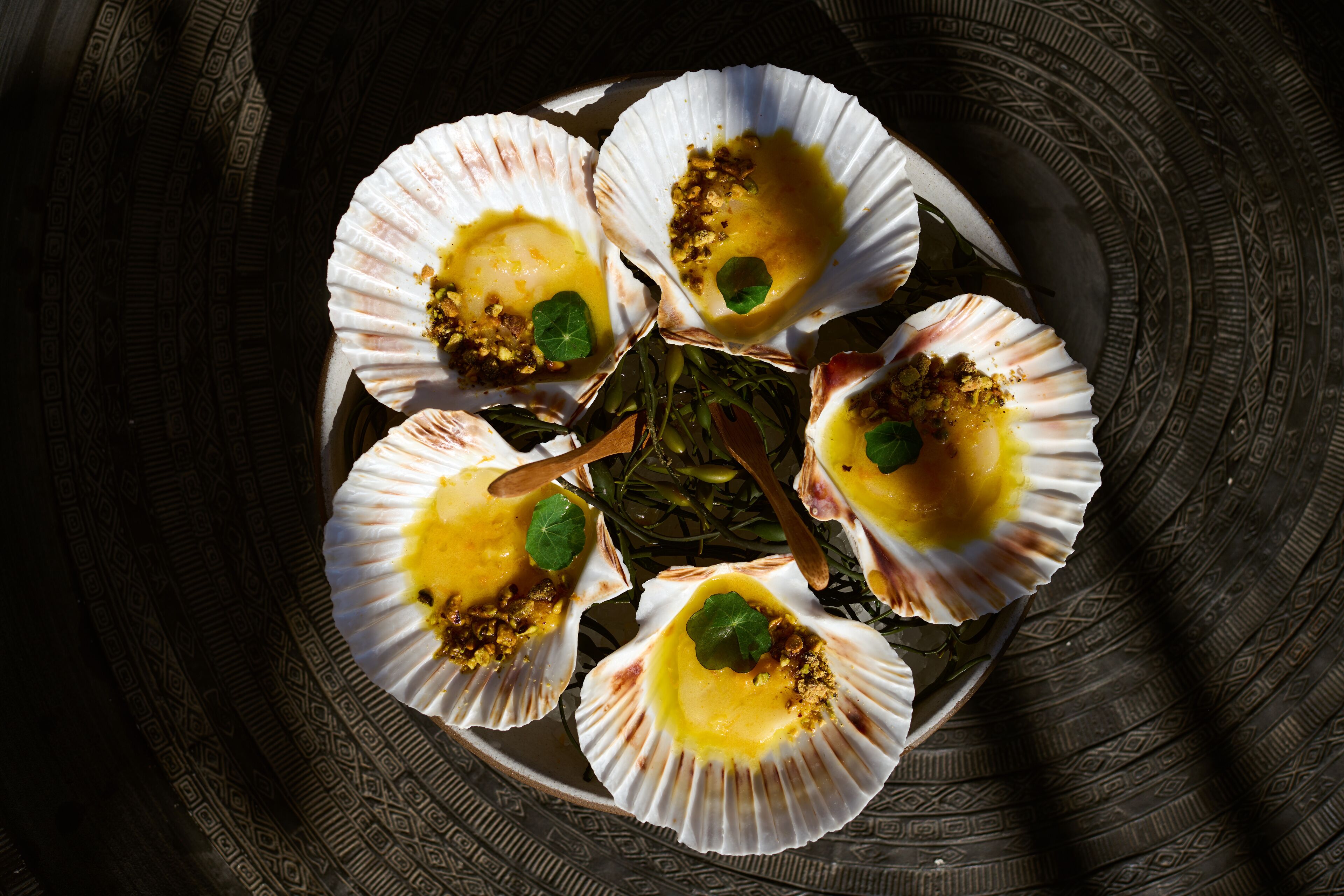 A plate of scallops with a garnish, arranged on a patterned surface.
