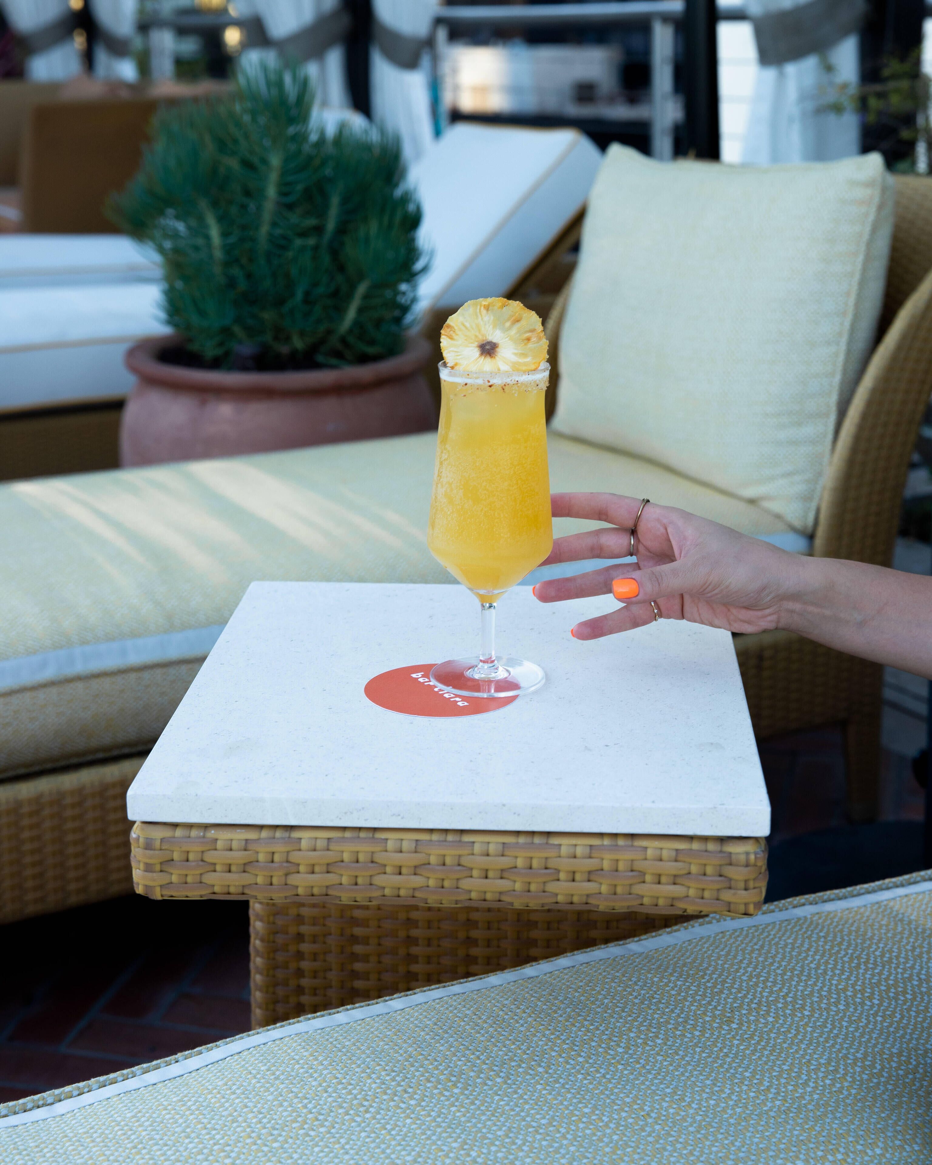 A cocktail glass with a pineapple garnish on a white coaster, placed on a small square table.