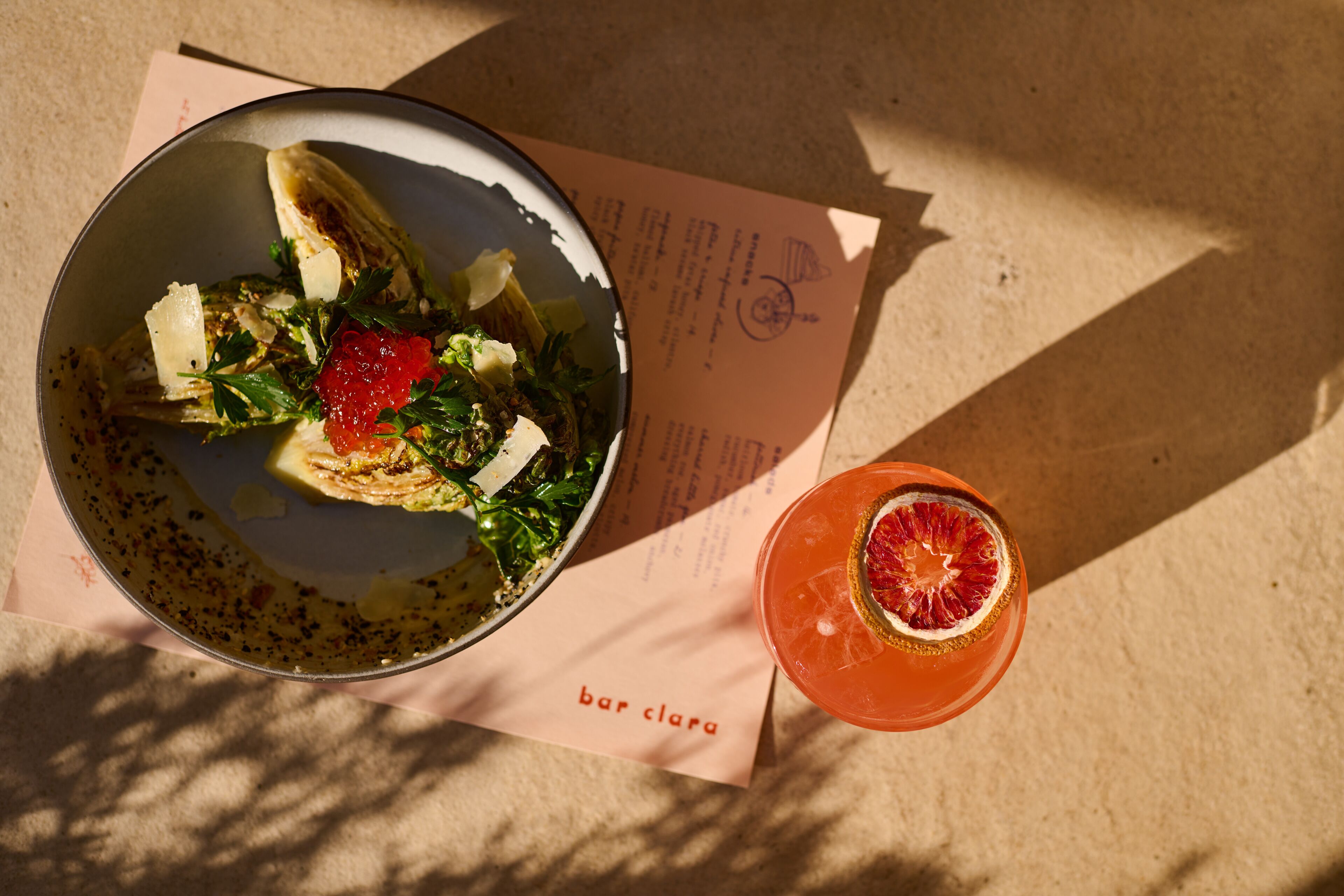 Una comida con ensalada y una bebida sobre una mesa con un menú.