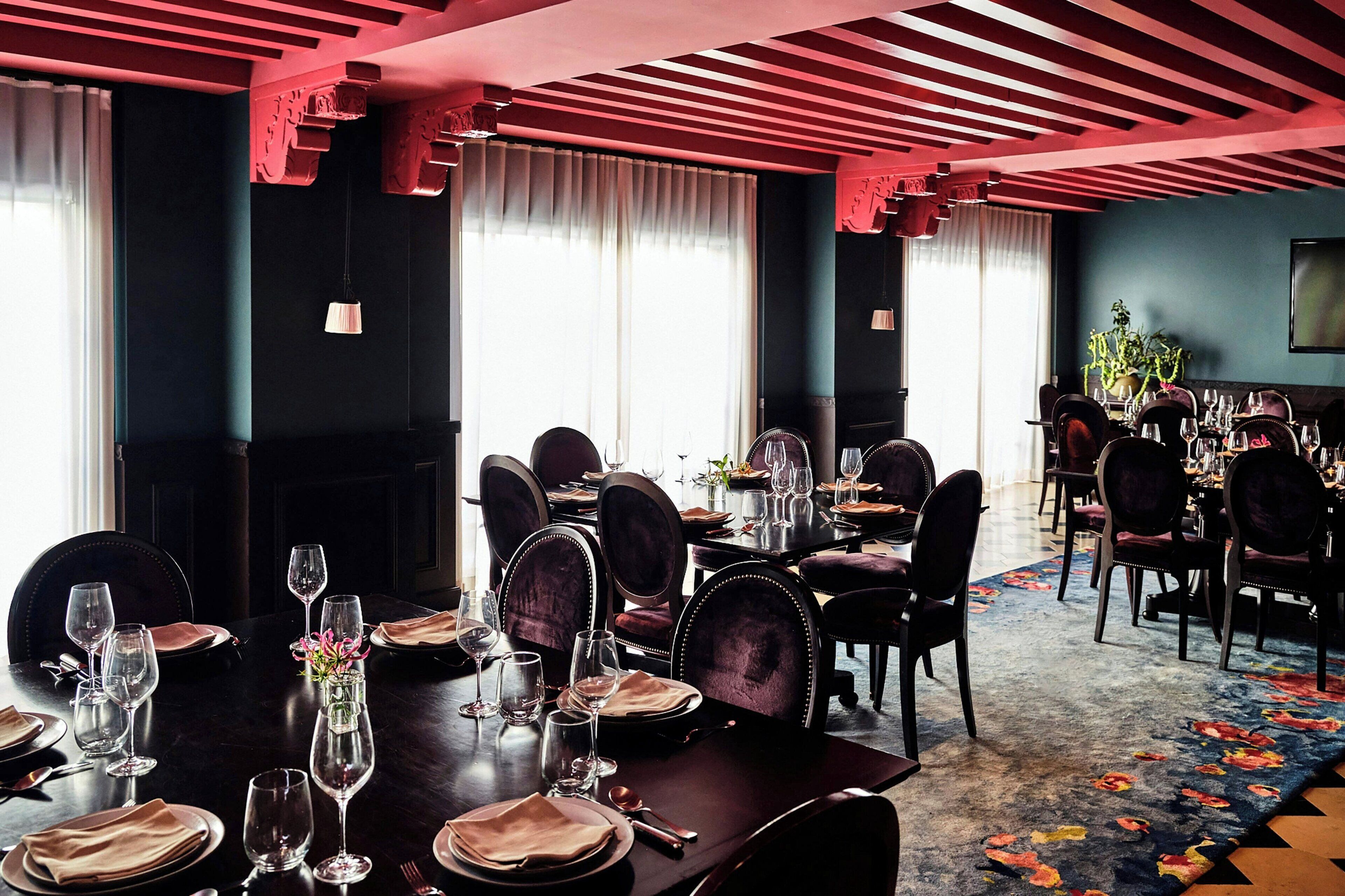 Comedor con varias mesas dispuestas para una comida, con muebles de madera oscura y una alfombra estampada.