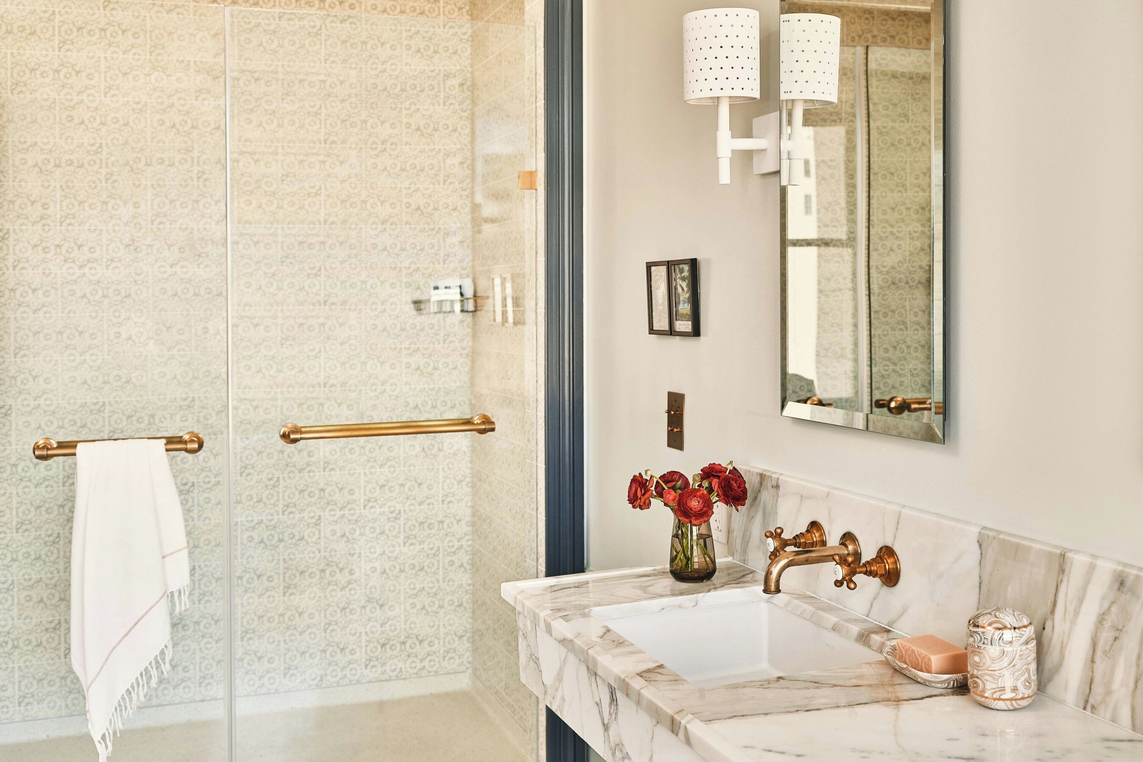 Un baño con lavamanos de mármol, grifo dorado y espejo con apliques de pared.