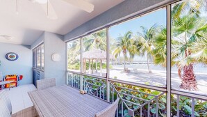 Ein Balkon mit Korbmöbeln, Blick auf Palmen und einen Strand, sowie ein Reetdachschirm.