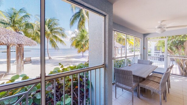 Ein Balkon mit Blick auf den Strand und Palmen, ein Korbstuhl-Tisch und -Stühle sowie ein Deckenventilator.