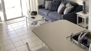 Ein modernes Wohnzimmer mit grauem Sofa, einem weißen Couchtisch und einer Küchenzeile mit Spüle und Herd.