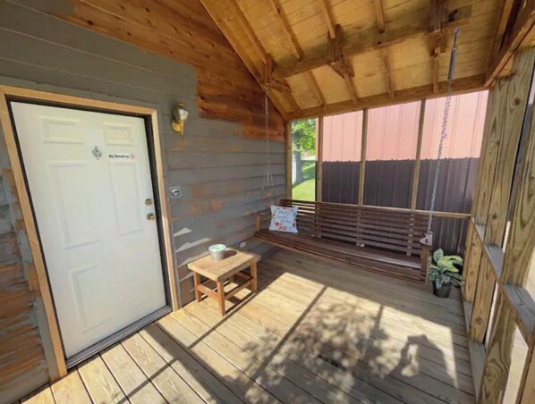 Una cabaña de madera con puerta, una mesita y un banco.