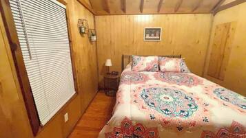Ein Schlafzimmer mit Holzwänden, einem Bett, einem Nachttisch mit Lampe und einem Fenster mit Jalousien.