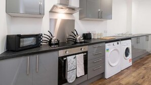 Una cucina moderna con mobili grigi, un forno a microonde, un piano cottura, una lavatrice e un ripiano con diversi oggetti da cucina.