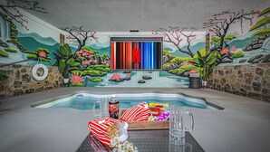 Een zwembadgedeelte met een muurschildering, een televisiescherm en een tafel met snacks en drankjes.