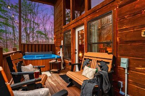 A wooden cabin with a hot tub, outdoor seating, and large windows.