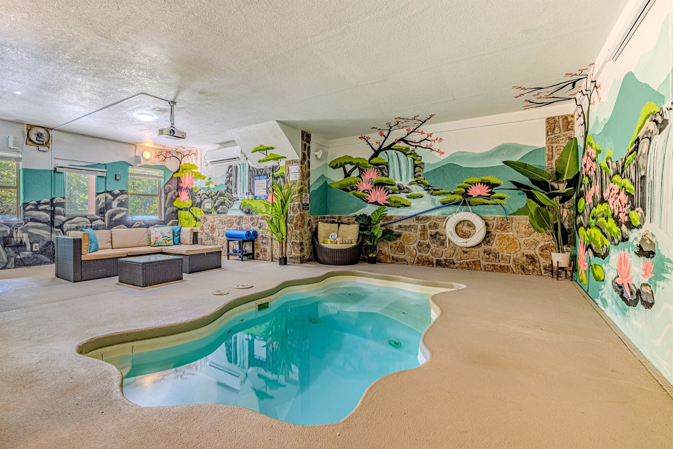 A spacious indoor pool area with a stone wall mural, comfortable seating, and a ceiling projector.