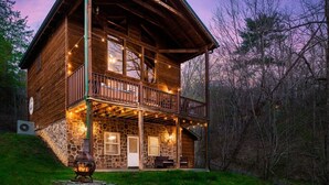 Een houten chalet met een stenen fundering, een balkon en lichtjes.