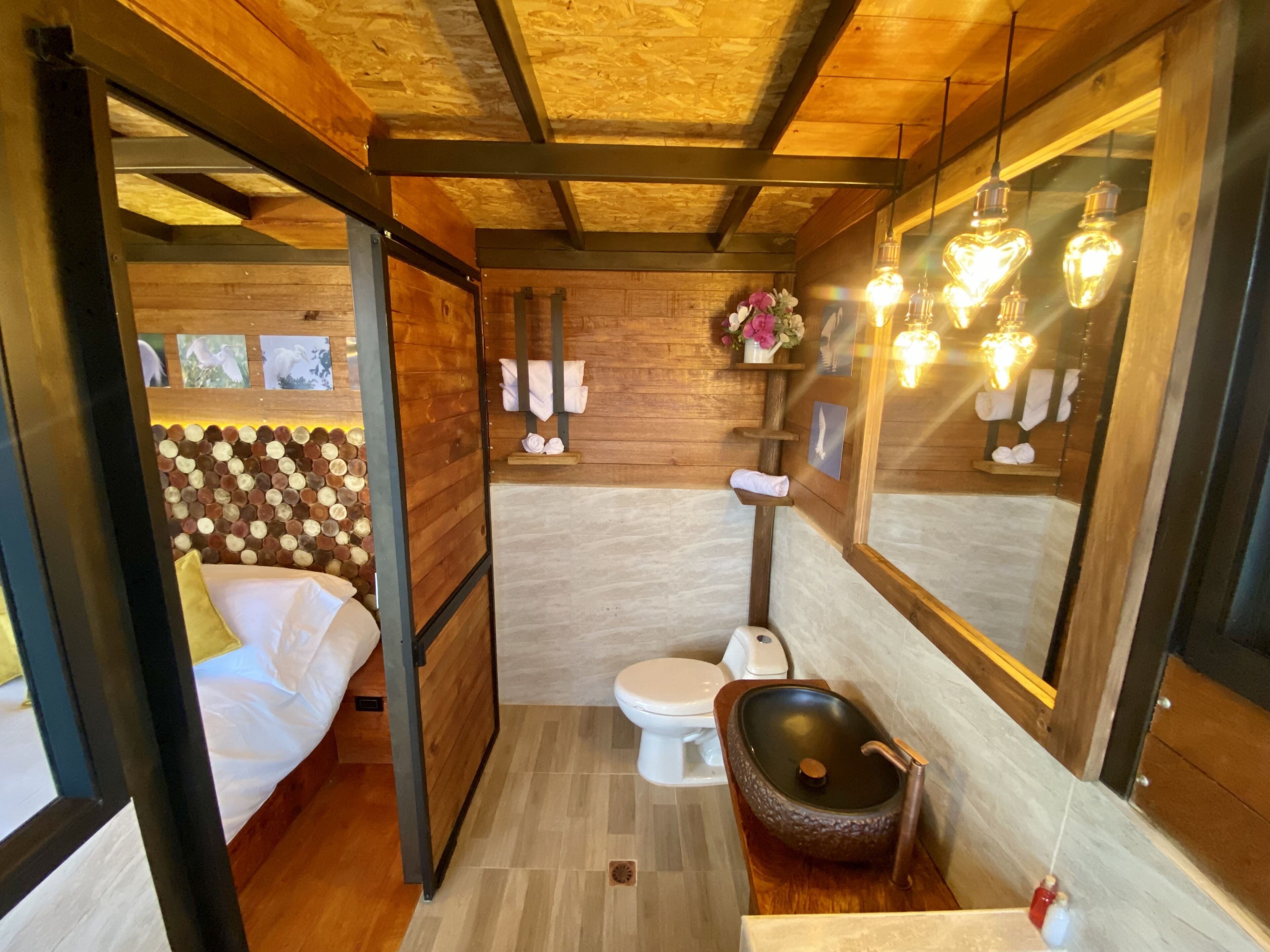 A compact, modern bathroom with a wooden ceiling, a built-in toilet, a sink with a unique basin, and a shower area.
