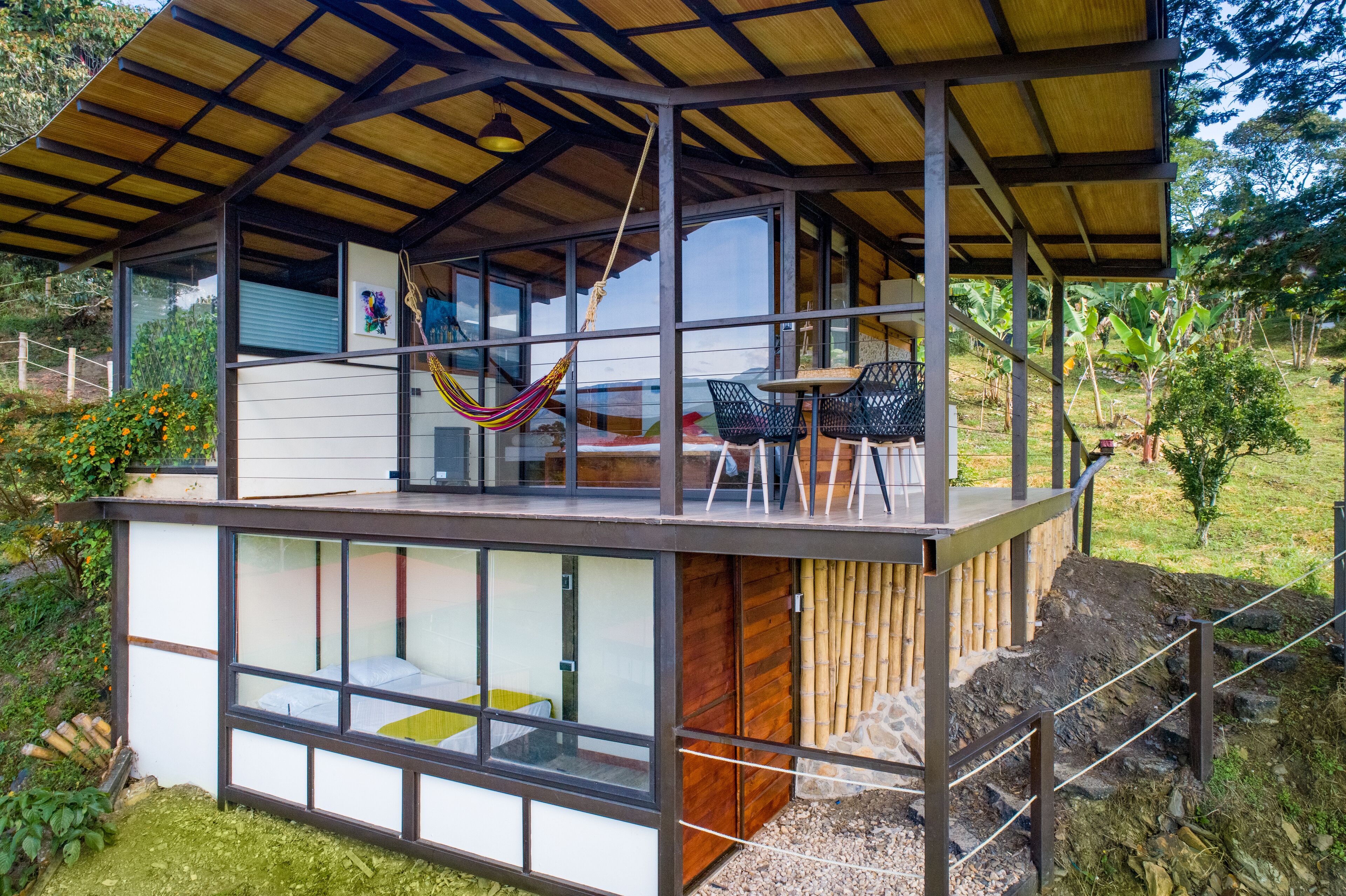 A modern house with a large glass window, a hammock, and a table.