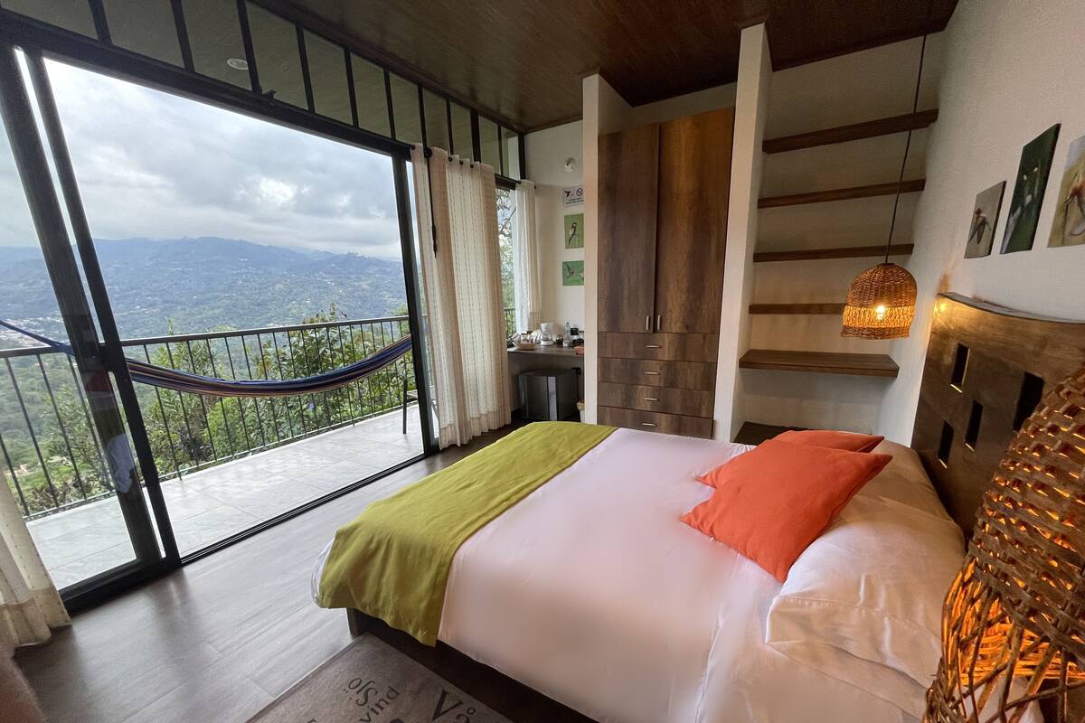 Ein Schlafzimmer mit einem großen Bett, Blick auf Berge von einem Balkon aus und einem Holzschrank.
