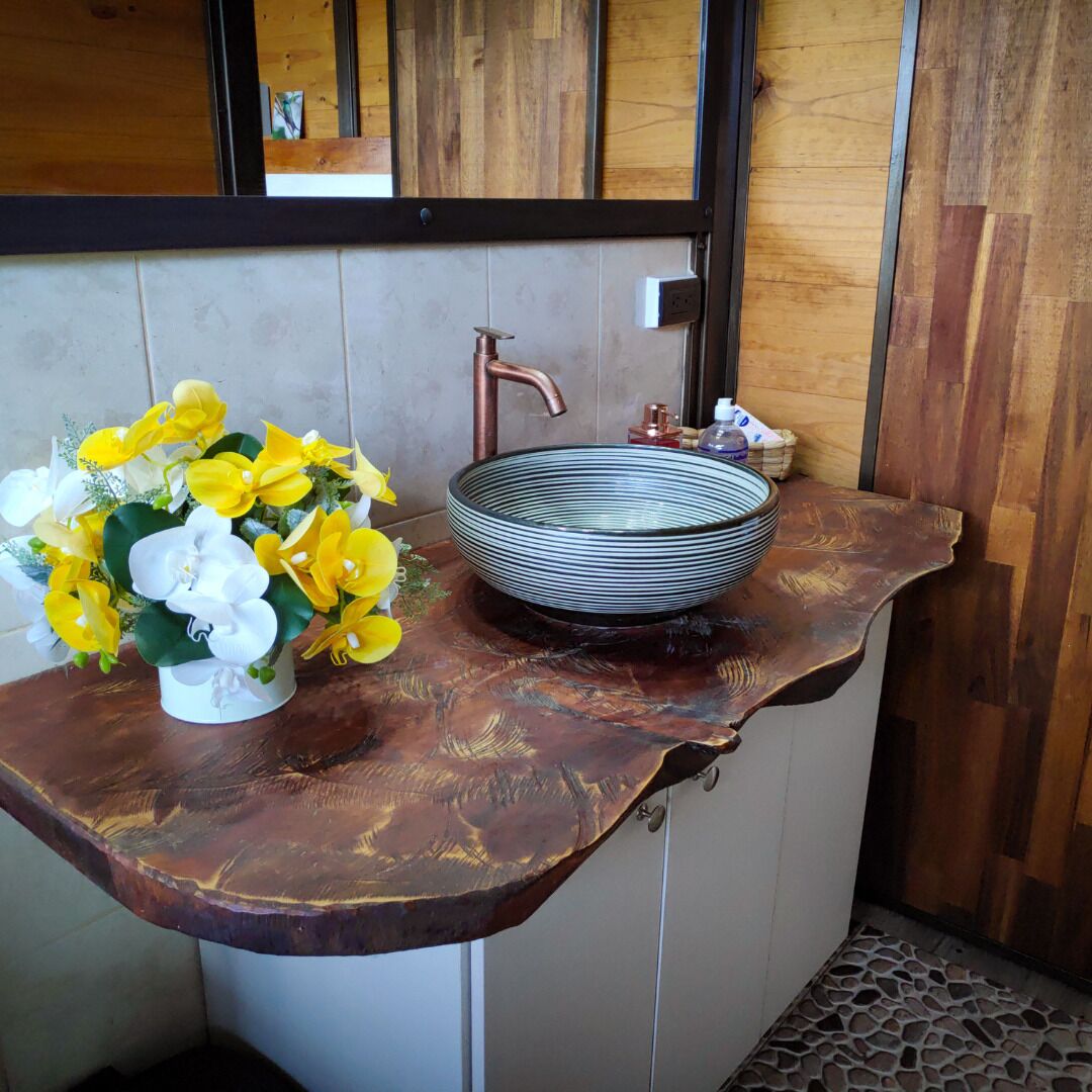 A bathroom with a wooden vanity, a copper faucet, and a large bowl sink.