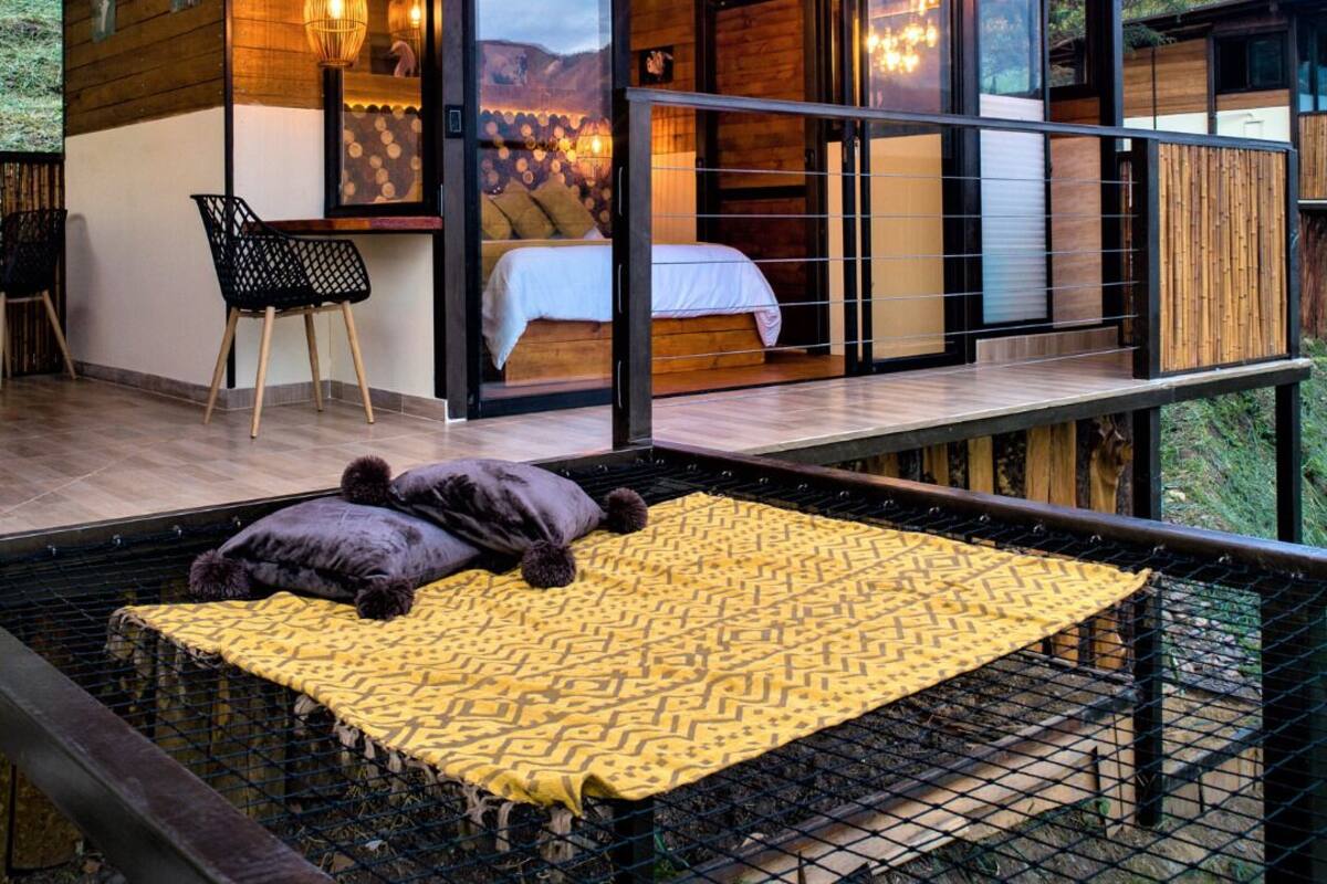 Ein modernes Schlafzimmer im Freien mit einem Bett, einem Sessel und einer gelb gemusterten Decke.