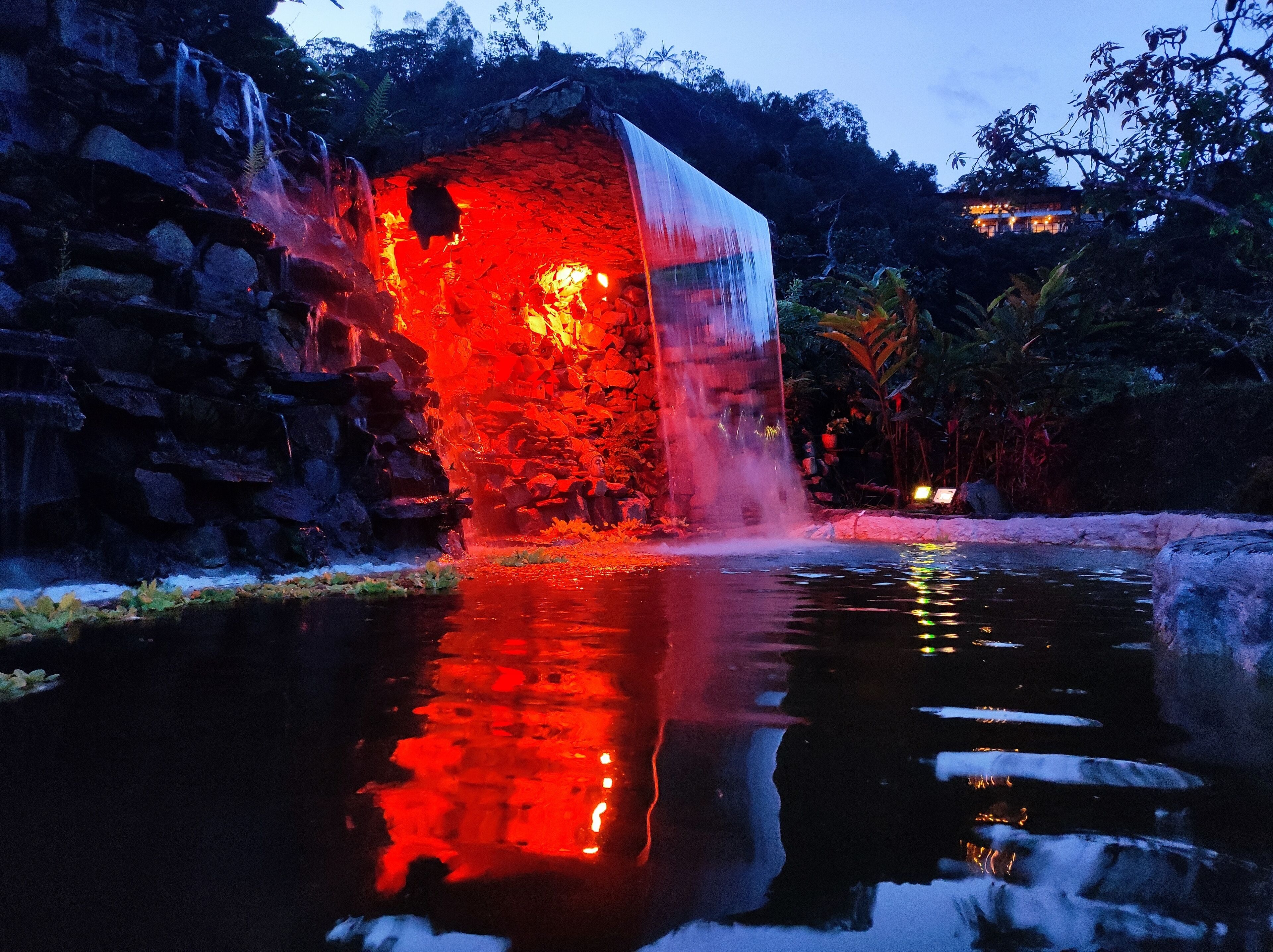 Ein Wasserfall stürzt in einen spiegelnden Teich, umgeben von felsigem Gelände und Vegetation.