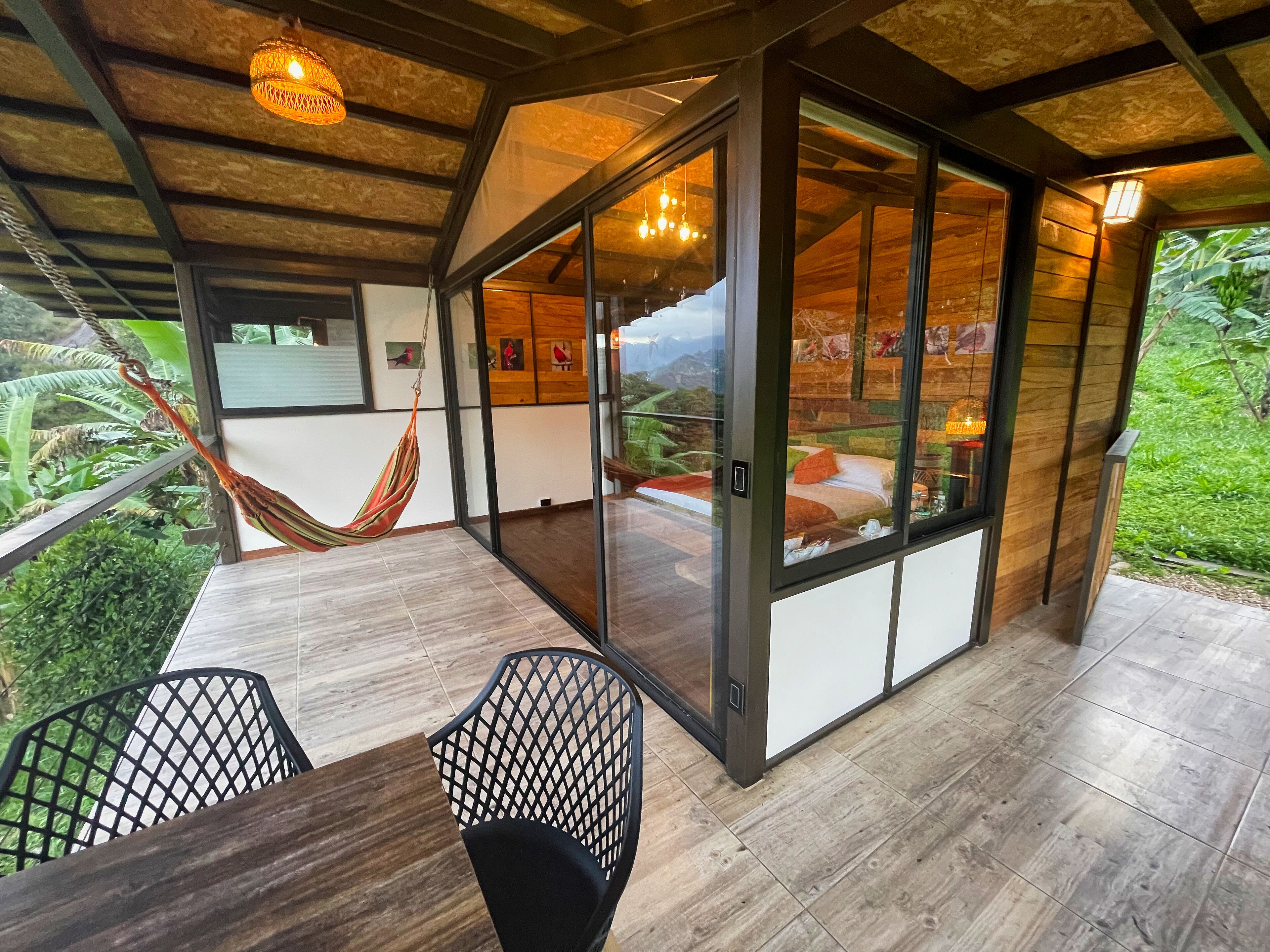 A modern room with a large sliding glass door leading to a balcony, a hammock, and a dining area with a table and chairs.