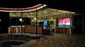 An outdoor bar area with a stone seating area, a counter with a TV screen, and string lights. - Natubri Ecohotel (San Francisco)