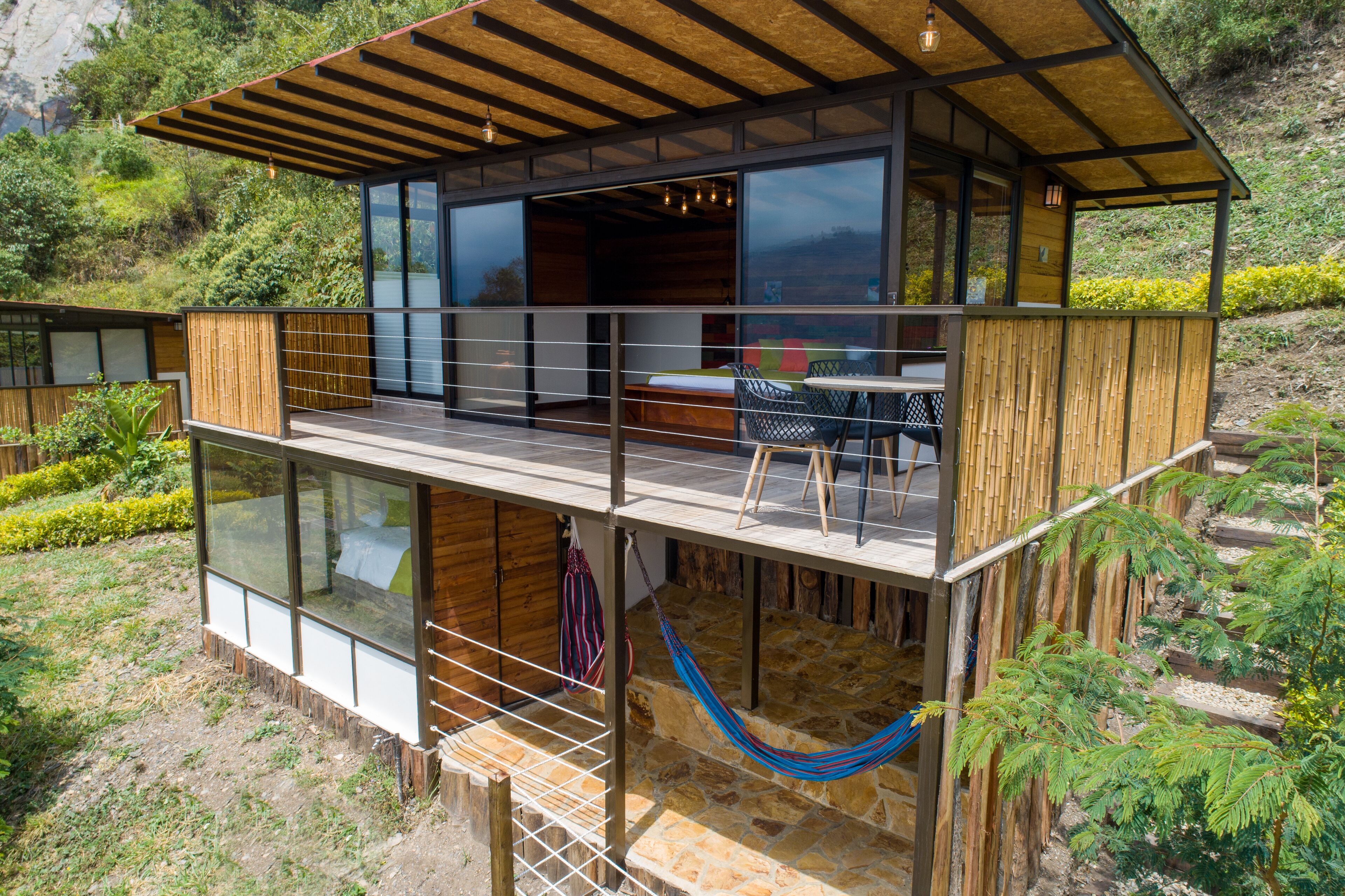 A modern, multi-level wooden cabin with glass walls, a balcony, and a hammock.