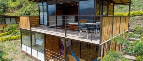 A modern, multi-level wooden cabin with glass walls, a balcony, and a hammock.