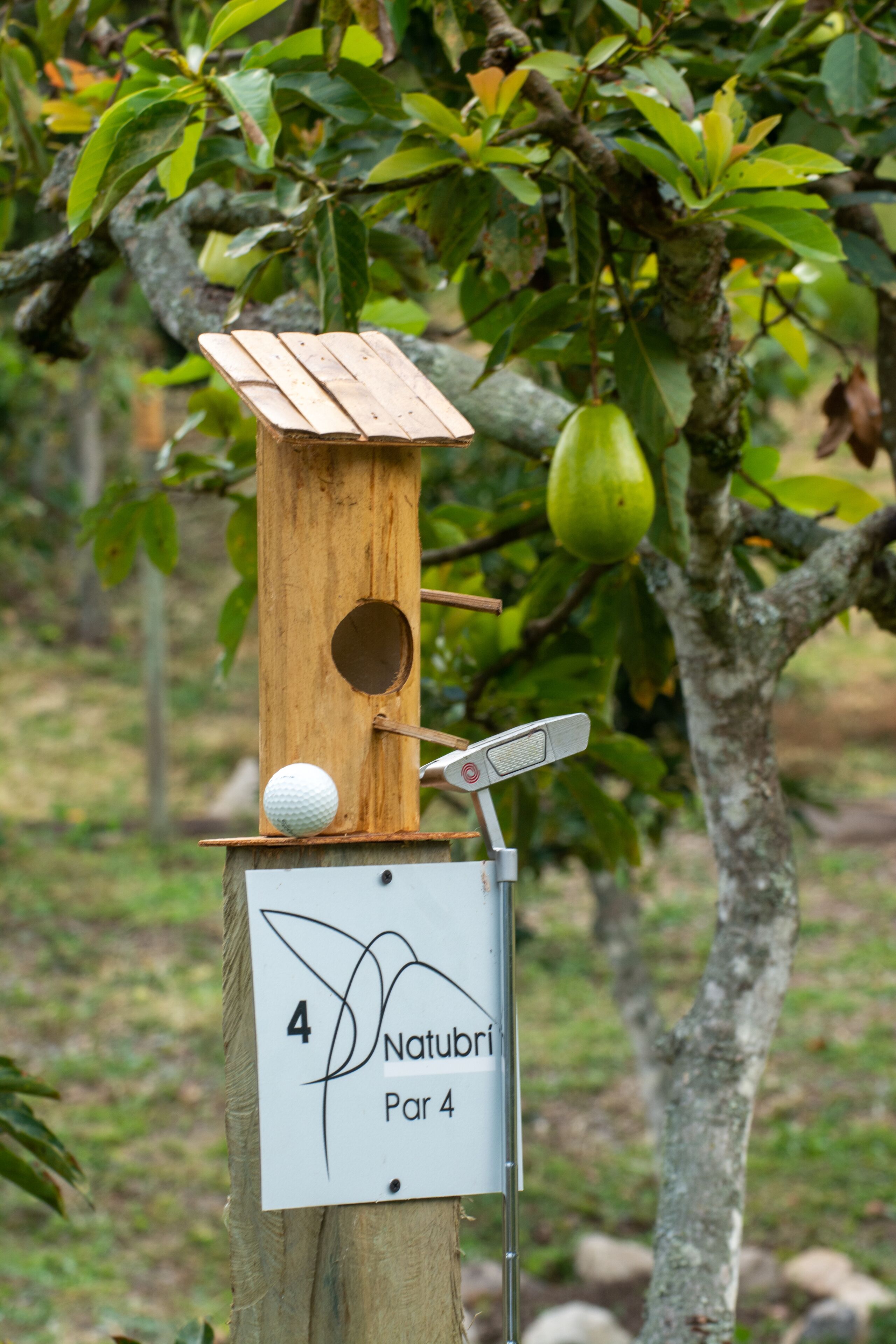 A wooden birdhouse with a white sign below it.