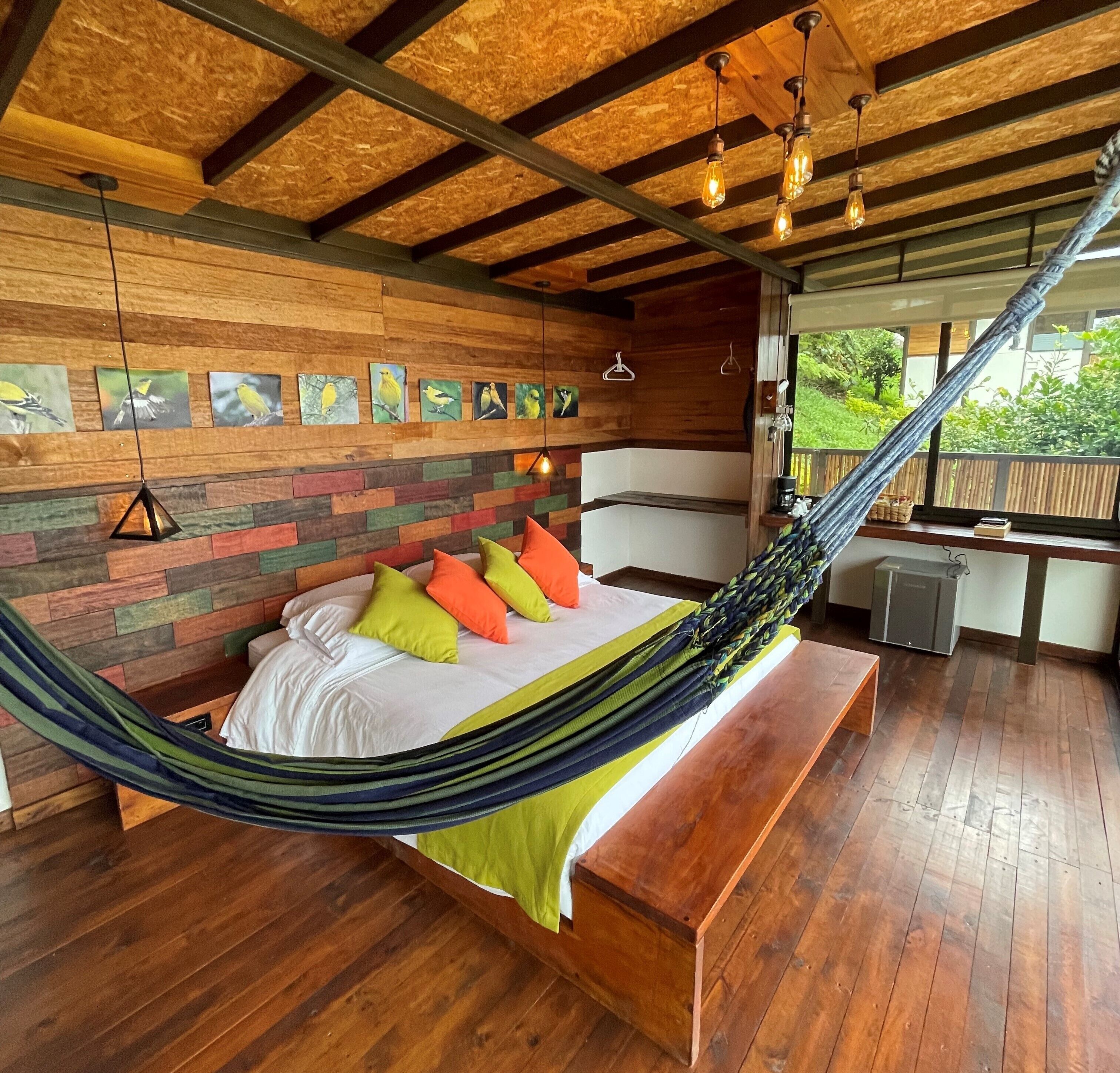 Una hamaca con almohadones coloridos, vigas de madera y una pared de madera con pinturas de pájaros.