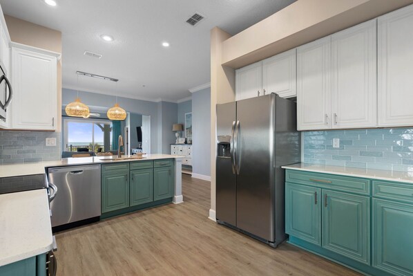 A modern kitchen with teal cabinetry, stainless steel appliances, and a large island.