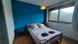 Een slaapkamer met een bed, nachtkastje, raam met uitzicht op bergen en een hanglamp.
