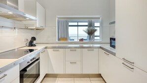 A modern kitchen with white cabinetry, a stainless steel range hood, a built-in oven, and a window with curtains. - Seafront apartment in the heart of Sliema MMAI2 (Sliema)